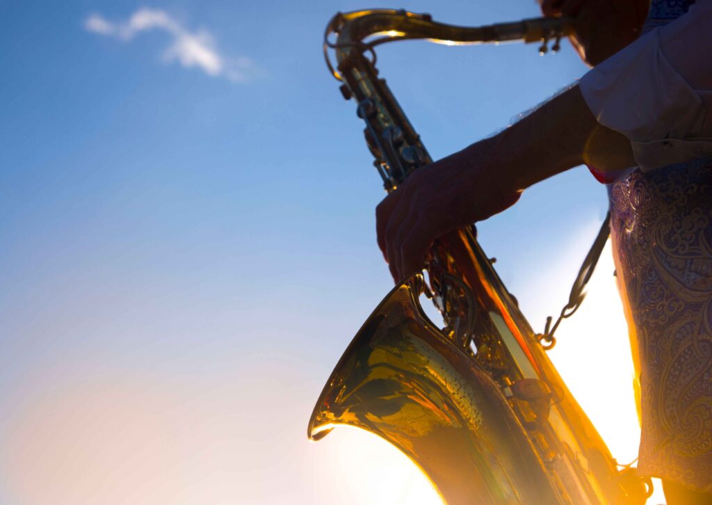 silhouette of a musician playing a baritone saxophone against a turquoise sky