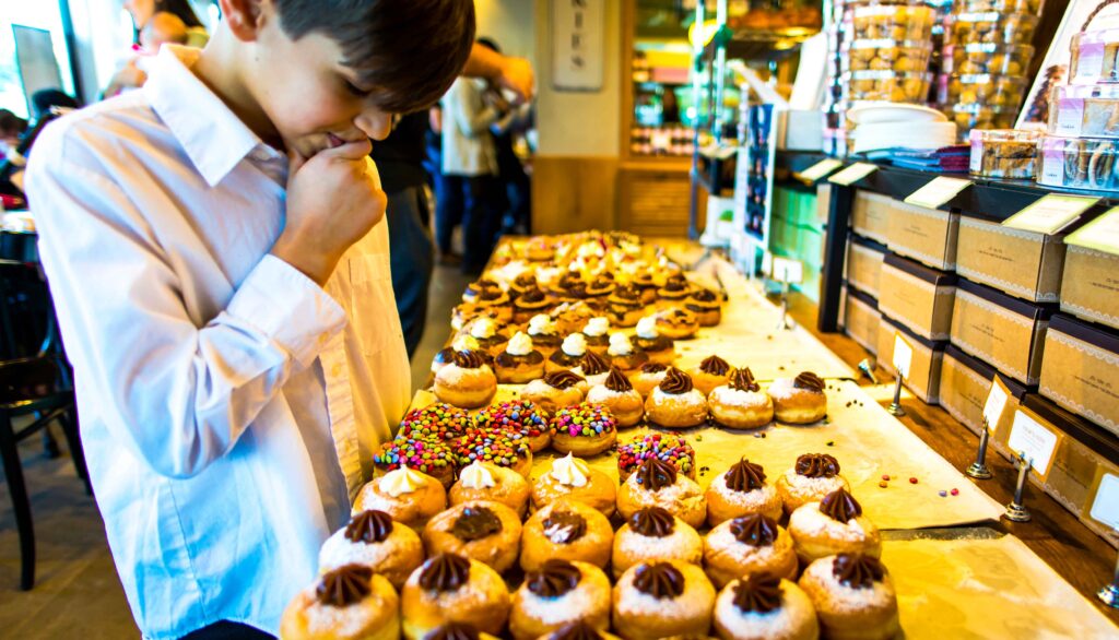 Boy choosing sufganiyot which are traditional Hanukkah doughnuts in a bakery